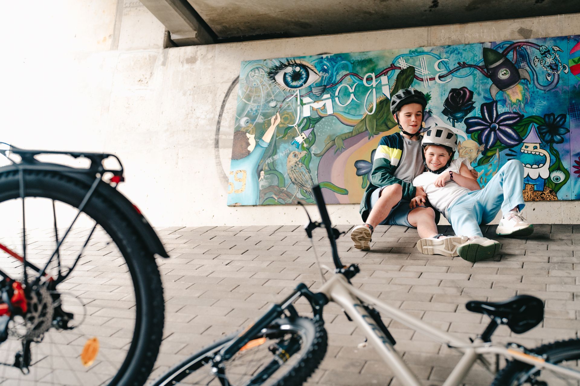 Kindjes met hun fiets onder een brug met graffiti op de achtergrond